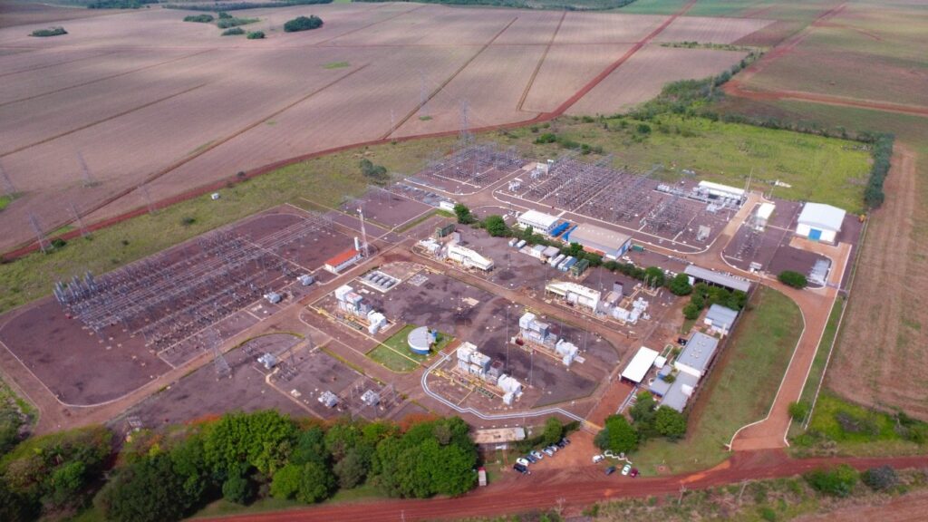 Usina termoelétrica liberando fumaça em meio a uma cidade ao anoitecer.